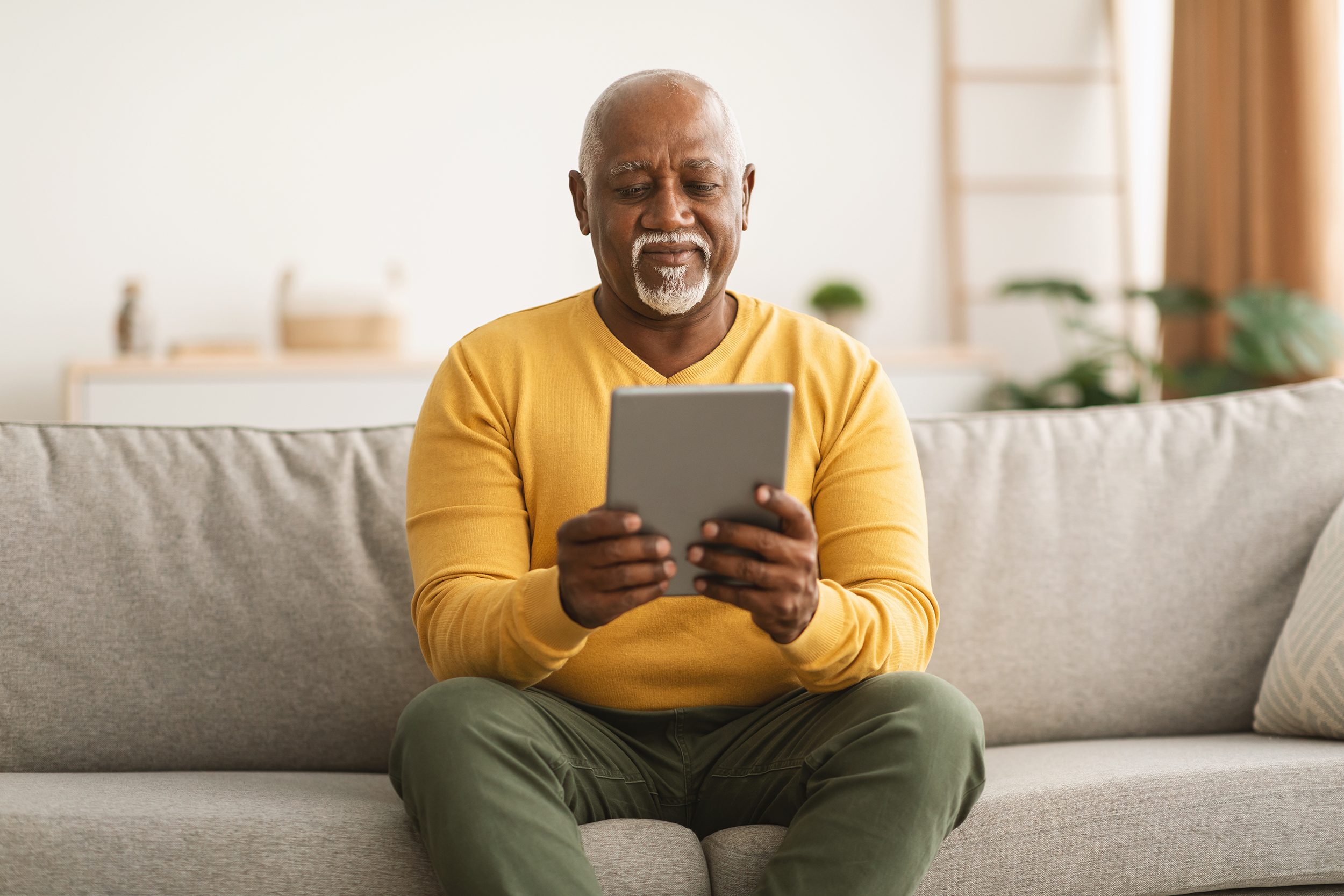 Older Man On Tablet Yellow Jumper Web